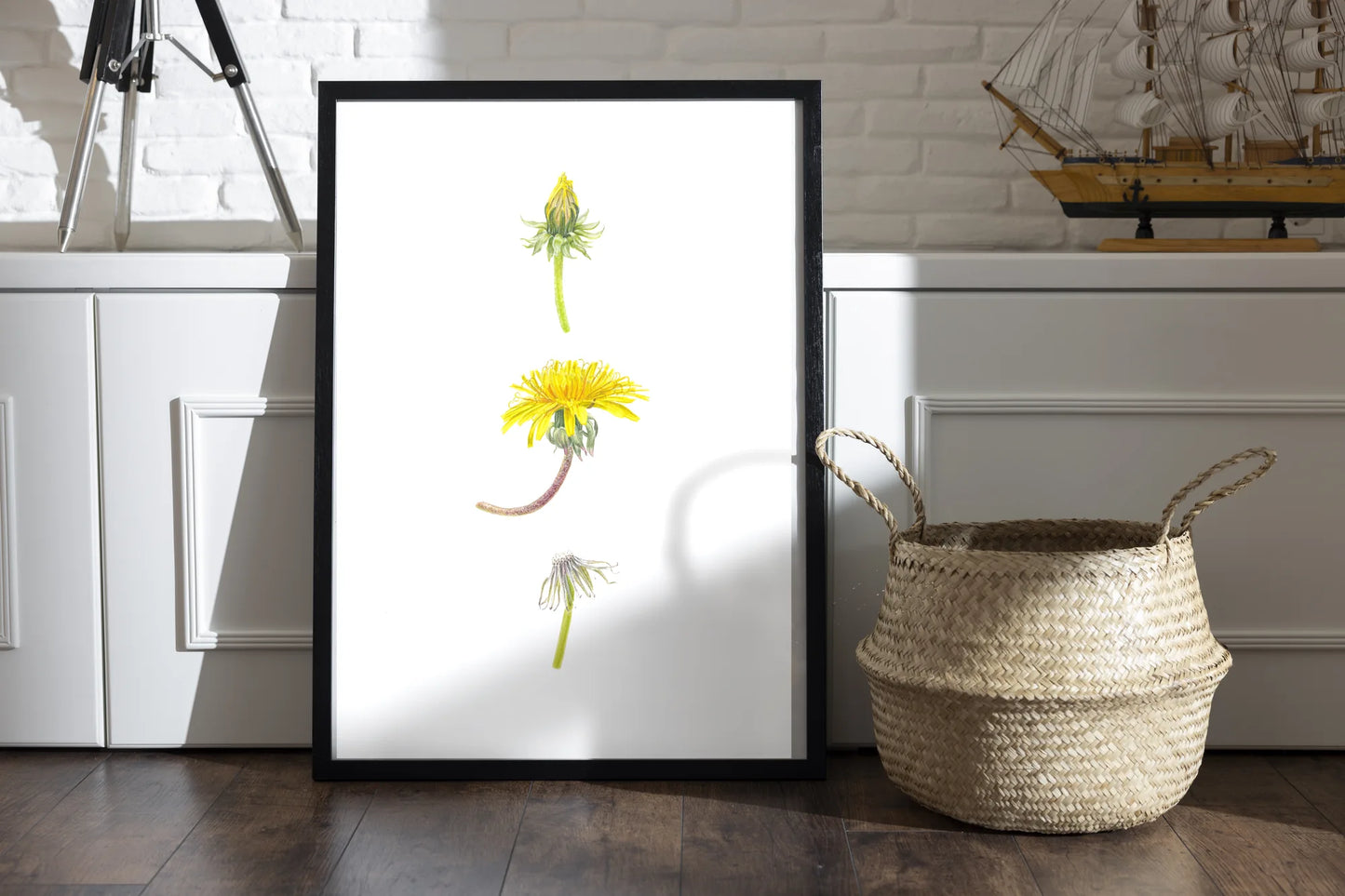 Löwenzahn Kunstdruck im schwarzen Rahmen auf Holzboden neben Weidenkorb – Aquarellillustration von Taraxacum officinale | Animis
