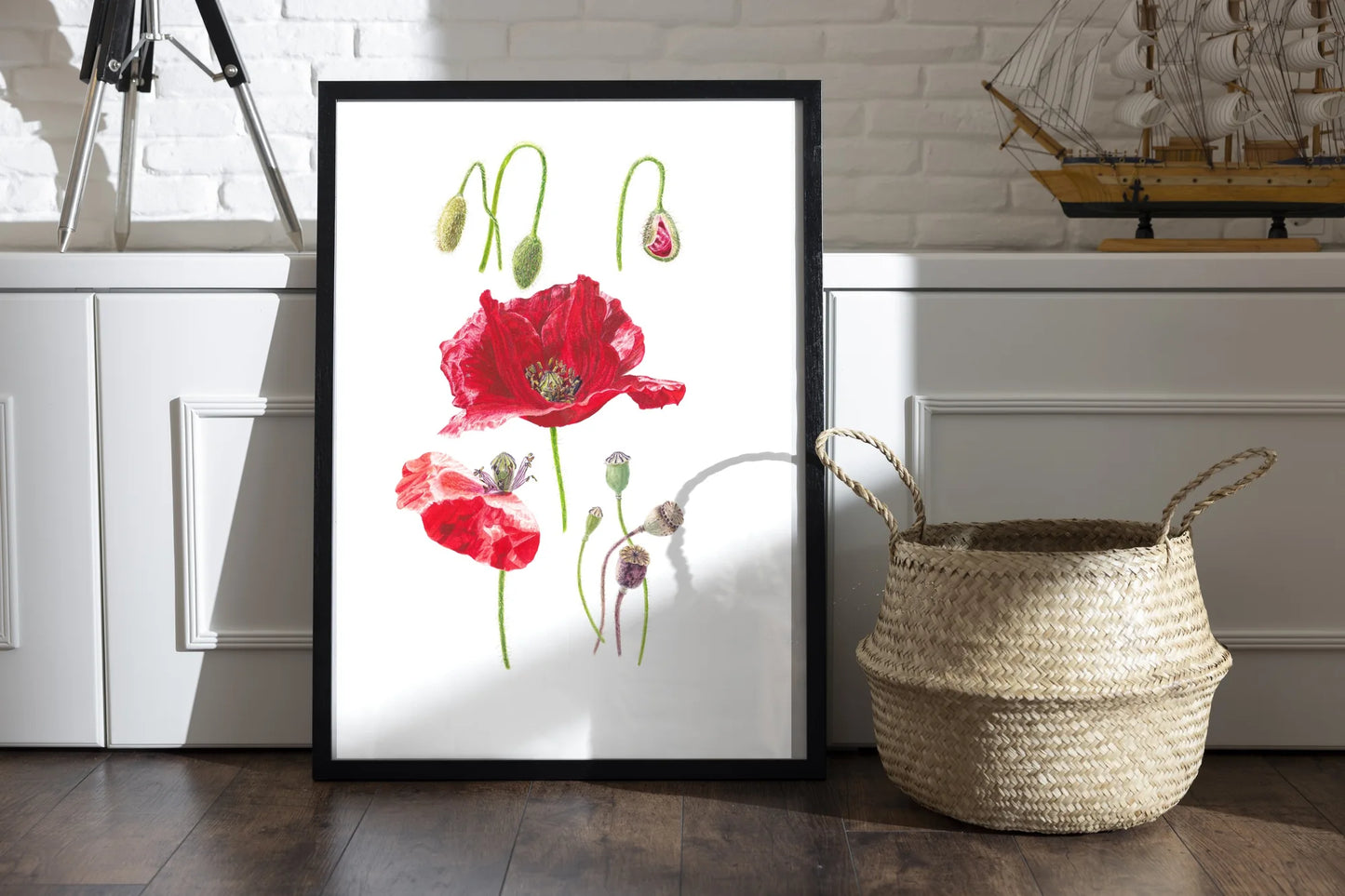 Mohn Kunstdruck im schwarzen Rahmen auf Holzboden neben Weidenkorb – Aquarellillustration von Papaver rhoeas mit Blüten und Knospen | Animis